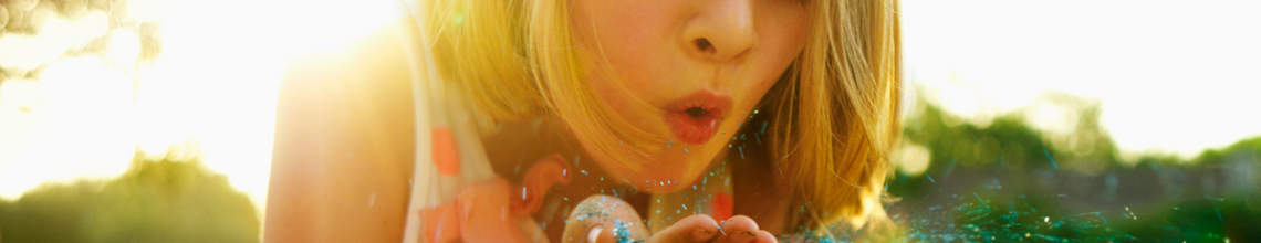 Young girl blowing glitter from cupped hands