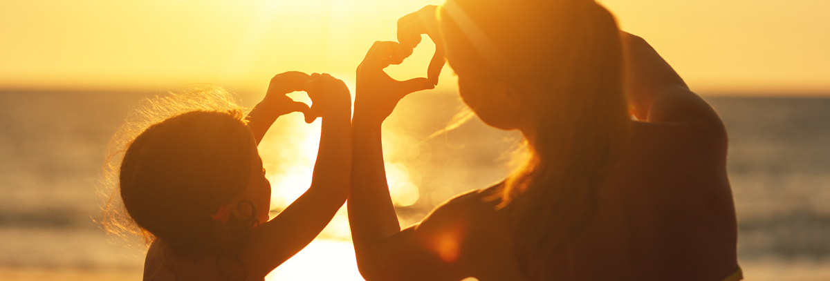 Une mère et sa fille mettent leurs mains en forme de cœur en regardant le coucher de soleil. 